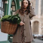 A woman in a brown coat carries a wicker basket of green vegetables while strolling through Erfurt, Germany.