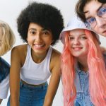 Low angle of group of cheerful multiethnic teenager friends standing together against white background and looking at camera