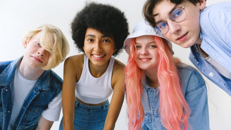 Low angle of group of cheerful multiethnic teenager friends standing together against white background and looking at camera