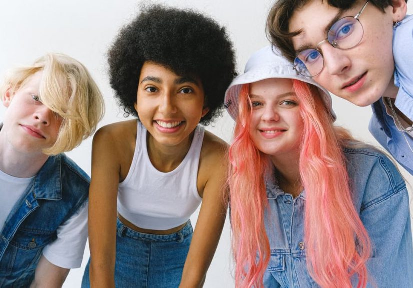 Low angle of group of cheerful multiethnic teenager friends standing together against white background and looking at camera